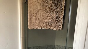 A glass-enclosed shower with a tiled floor and a metal handle.