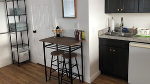 A kitchen with a wooden table, two stools, a wine bottle, and a mirror on the wall.