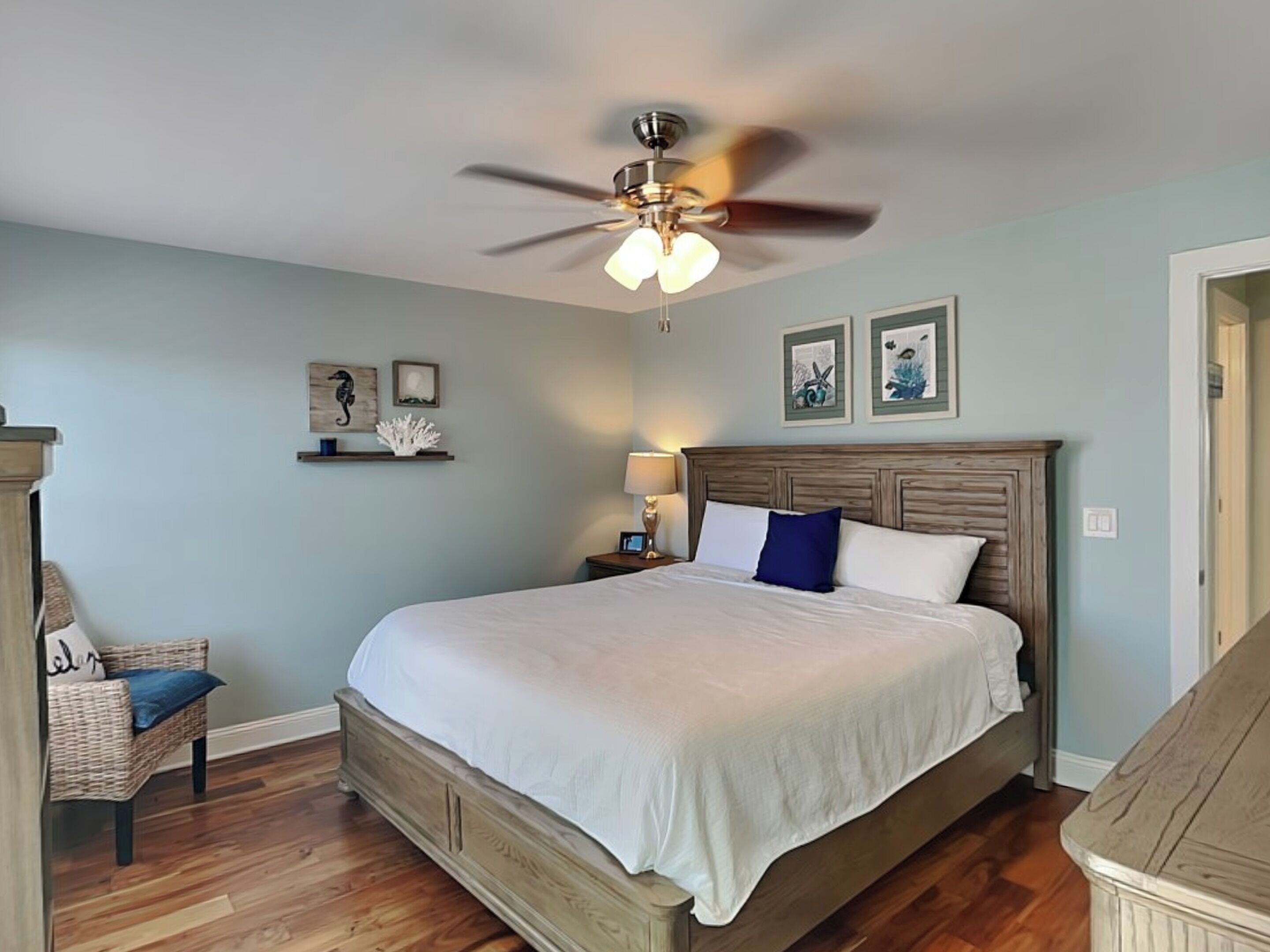 A bedroom with a wooden bed, a ceiling fan, and wall-mounted artwork.