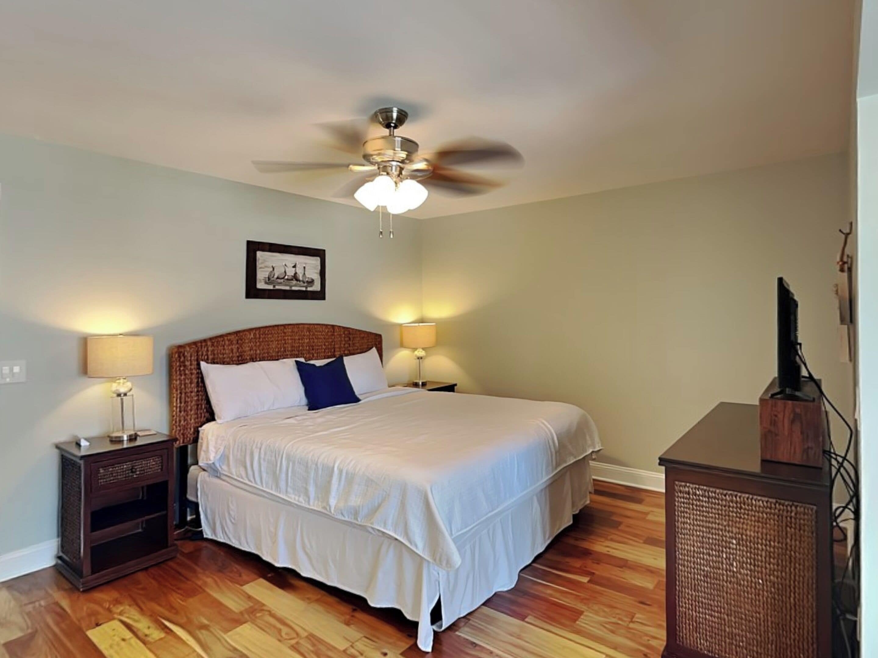 A bedroom with a bed, two bedside tables, a ceiling fan, and a television on a stand.