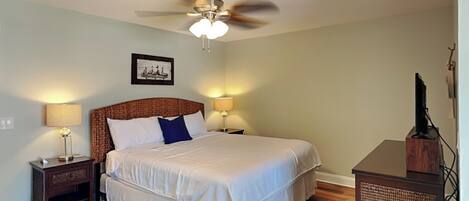 A bedroom with a bed, two bedside tables, a ceiling fan, and a television on a stand.