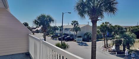 A balcony with a white railing overlooking a street lined with palm trees and parked cars.