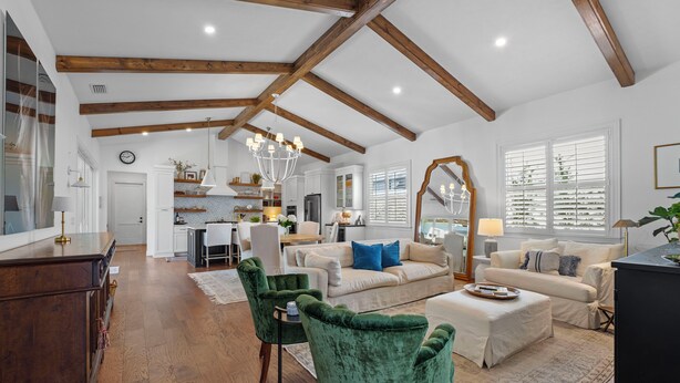 Ein großzügiger Wohnraum mit hohen Decken, Holzbalken, einem großen Kronleuchter und einer gemütlichen Sitzecke mit Sofa und Sesseln.