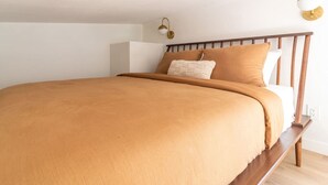 A bedroom with a wooden bed frame, a beige bedspread, and a white pillow.