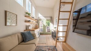 A compact living space with a sofa, a patterned rug, a TV mounted on the wall, and a wooden ladder.