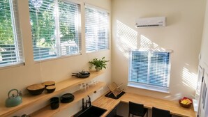 Une cuisine de taille réduite, dotée de plans de travail en bois, d’un évier noir et d’une fenêtre avec des stores.
