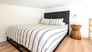 A neatly made bed with a striped bedspread, a dark headboard, and a wooden side table with a lamp. - Extended Stay Retreat: Cozy yet Spacious Tiny Gem! (Austin)
