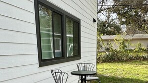 A patio with a table and two chairs, a wooden deck, and a white house with a black window frame. - Extended Stay Retreat: Cozy yet Spacious Tiny Gem! (Austin)