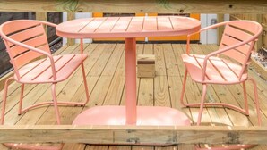 Een ronde tafel met twee roze stoelen op een houten terras.