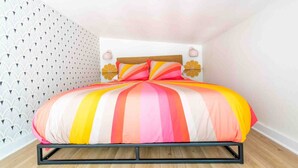 Een bed met een kleurrijke gestreepte spreidek en een kamer met een behanget en een houten vloer.