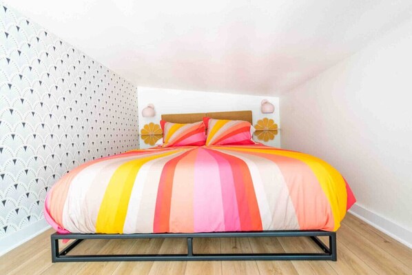 A bed with a colorful striped bedspread in a room with a patterned wall and a wooden floor. - Unique Vintage Vibes - Cozy Tiny Home close to UT! (Austin)