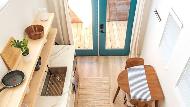 A compact kitchen with a wooden countertop, a sink, and a dining area with a striped tablecloth. - Cozy & Bright Mid-Century Gem in Eastside Action! (Austin)