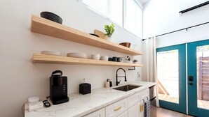 A modern kitchen with white cabinetry, a black coffee maker, and wooden shelves above the counter. - Cozy & Bright Mid-Century Gem in Eastside Action! (Austin)