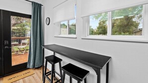 A room with a black desk, two black stools, a clock, and a window with blinds.