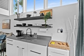 A modern kitchen with white cabinets, a black countertop, and a built-in oven. There are shelves above the sink holding kitchenware and a potted plant. - Spacious & Bright w/ Deck - Walkable to 6th St! (Austin)