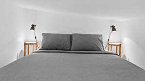 A minimalist bedroom with a large bed, two bedside tables, and two wall-mounted lamps.