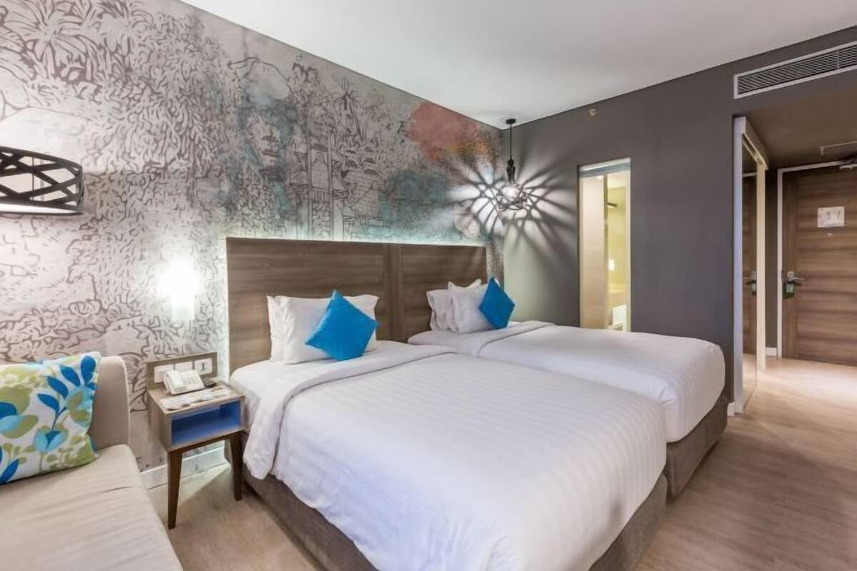 A hotel room with a large bed, a nightstand, a wall with a mural, and a door to the right.