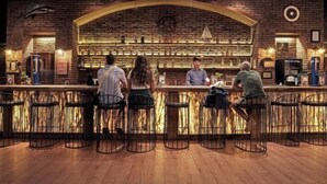 Zona de bar con pared de ladrillo, mostrador de madera y taburetes metálicos.