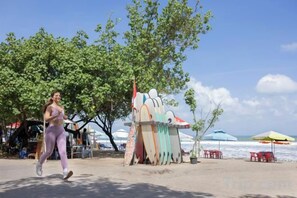 Une scène de plage avec une personne qui court, des planches de surf colorées et des parasols de plage.