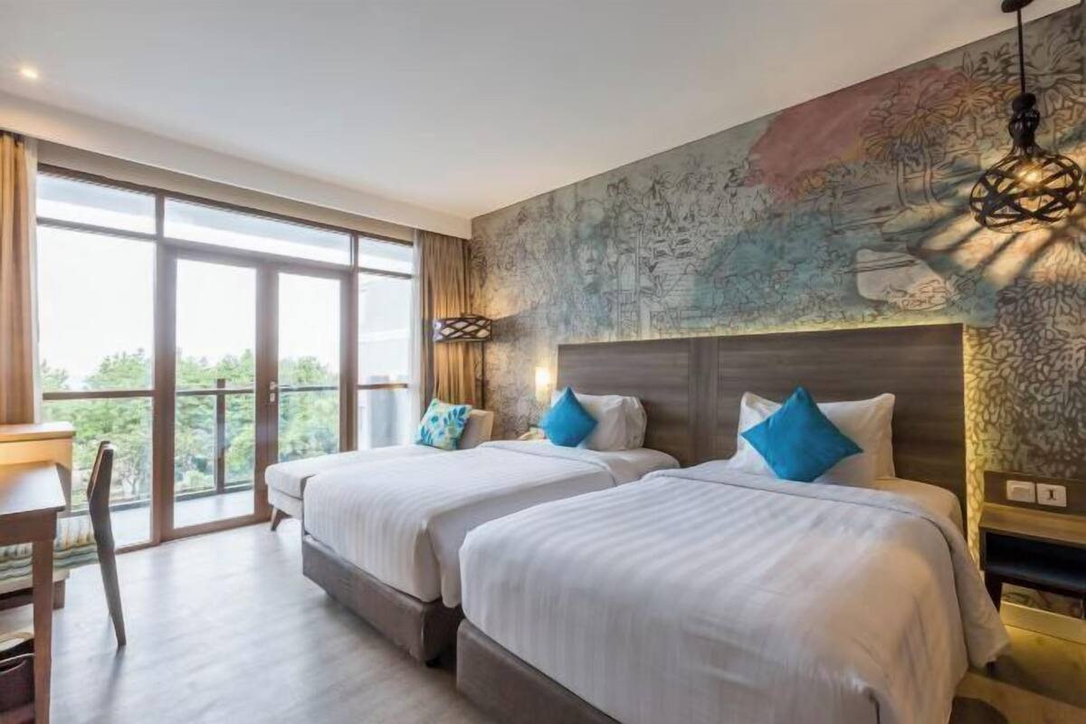 A hotel room with two beds, a desk, a chair, and a large window.