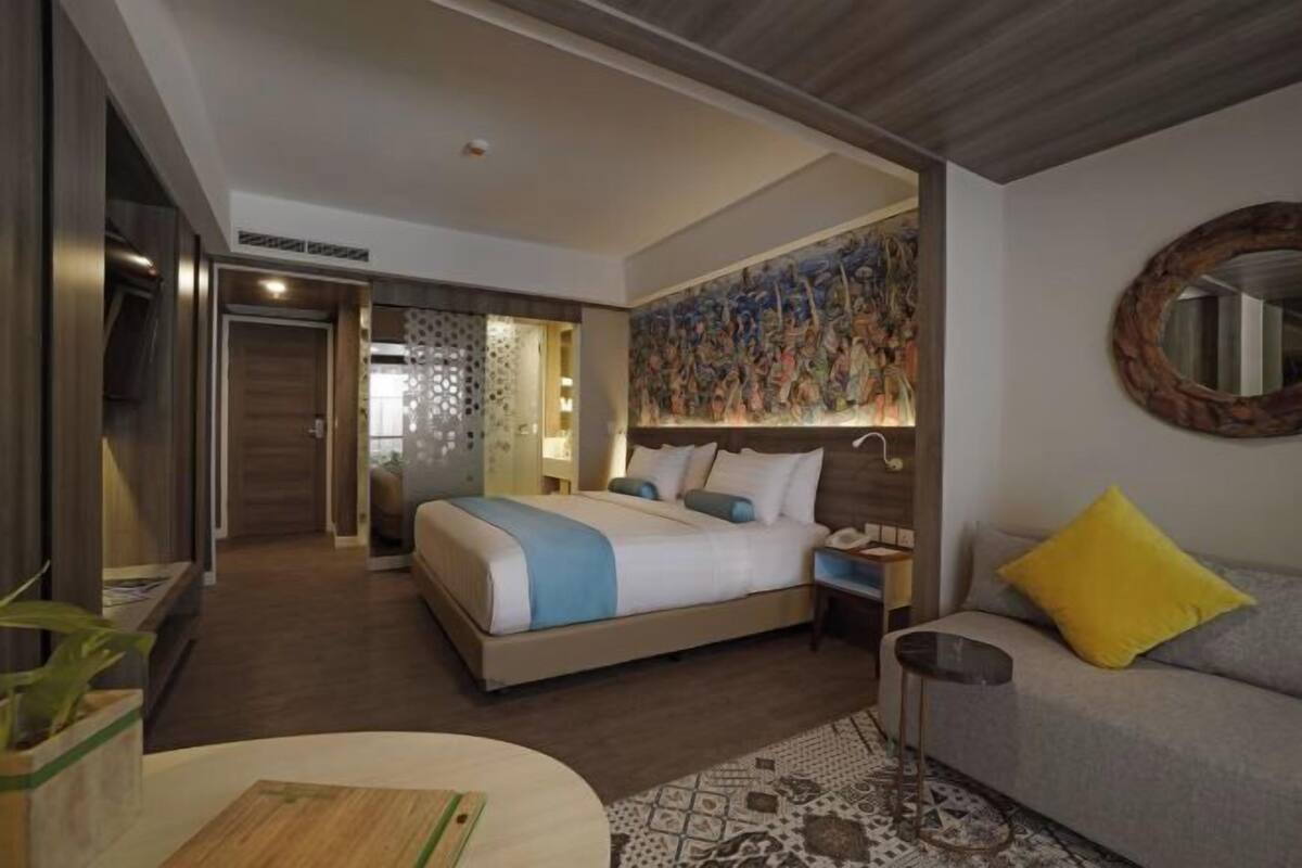 A modern hotel room with a large bed, a sofa, a round coffee table, and a decorative mirror.
