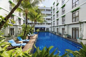 Un espace piscine d’hôtel doté d’une terrasse en bois, de chaises longues et d’une piscine à l’eau d’un bleu cristallin.