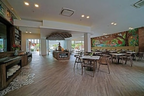 A spacious dining area with multiple tables and chairs, a central decorative piece, and a large mural on the wall. - Wyndham Garden Kuta Beach Bali (Bali)