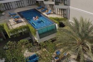 Un área de piscina en la azotea con sillones de descanso y una palmera.
