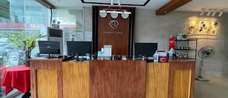 A reception desk with a wooden finish, two monitors, a plant, and a fan.