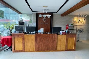 A reception desk with a wooden finish, two monitors, a plant, and a fan. - Diamond Spring Hotel Angeles (Angeles)