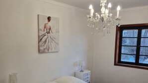 Un dormitorio con una cama grande, una mesita de noche con lámpara, un candelabro, una ventana con vistas y un cuadro en la pared.
