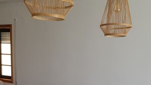 Un comedor con una mesa de madera, sillas blancas y dos lámparas colgantes de mimbre.