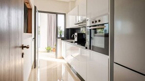 Een moderne keuken met witte kasten, roestvrijstalen apparatuur en een schuifdeur naar een balkon met planten.