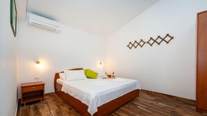A bedroom with a wooden bed, white bedding, a bedside table, a nightstand, and a wall-mounted air conditioner. - Beautiful apartment in Seline with WiFi (Seline)