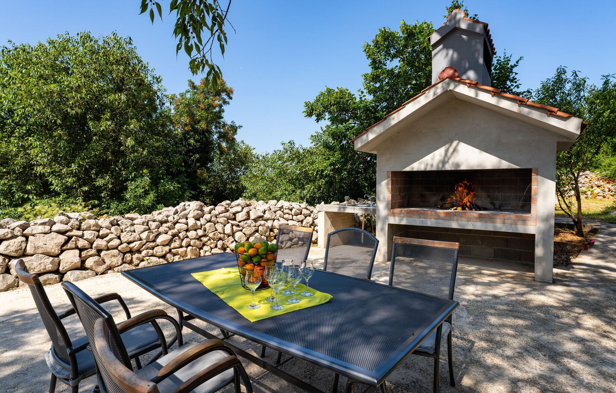 An outdoor patio with a stone wall, a metal table with chairs, and a brick oven.