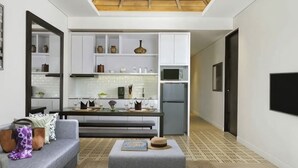 Un salon moderne avec un canapé gris, une table basse et un coin cuisine doté de meubles blancs et d’un four à micro-ondes.