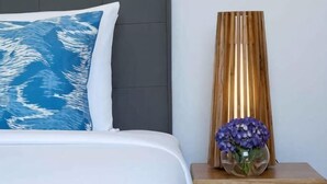 A bed with a white and blue pillow, a wooden nightstand with a vase of flowers, and a tall, narrow, golden-colored object. - Avani Seminyak Bali Resort (Bali)