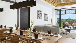 A dining area with a wooden table set for a meal, a sofa with cushions, and a balcony with a view. - Avani Seminyak Bali Resort (Bali)