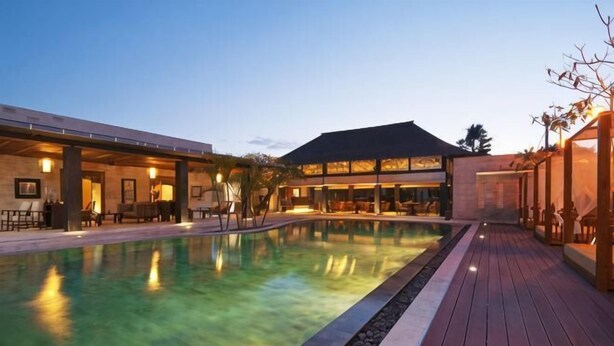 A swimming pool with a wooden deck, a building with a dark roof, and a clear sky. - Avani Seminyak Bali Resort (Bali)