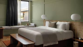 A bedroom with a bed, bench, bedside table, lamp, and window with curtains.