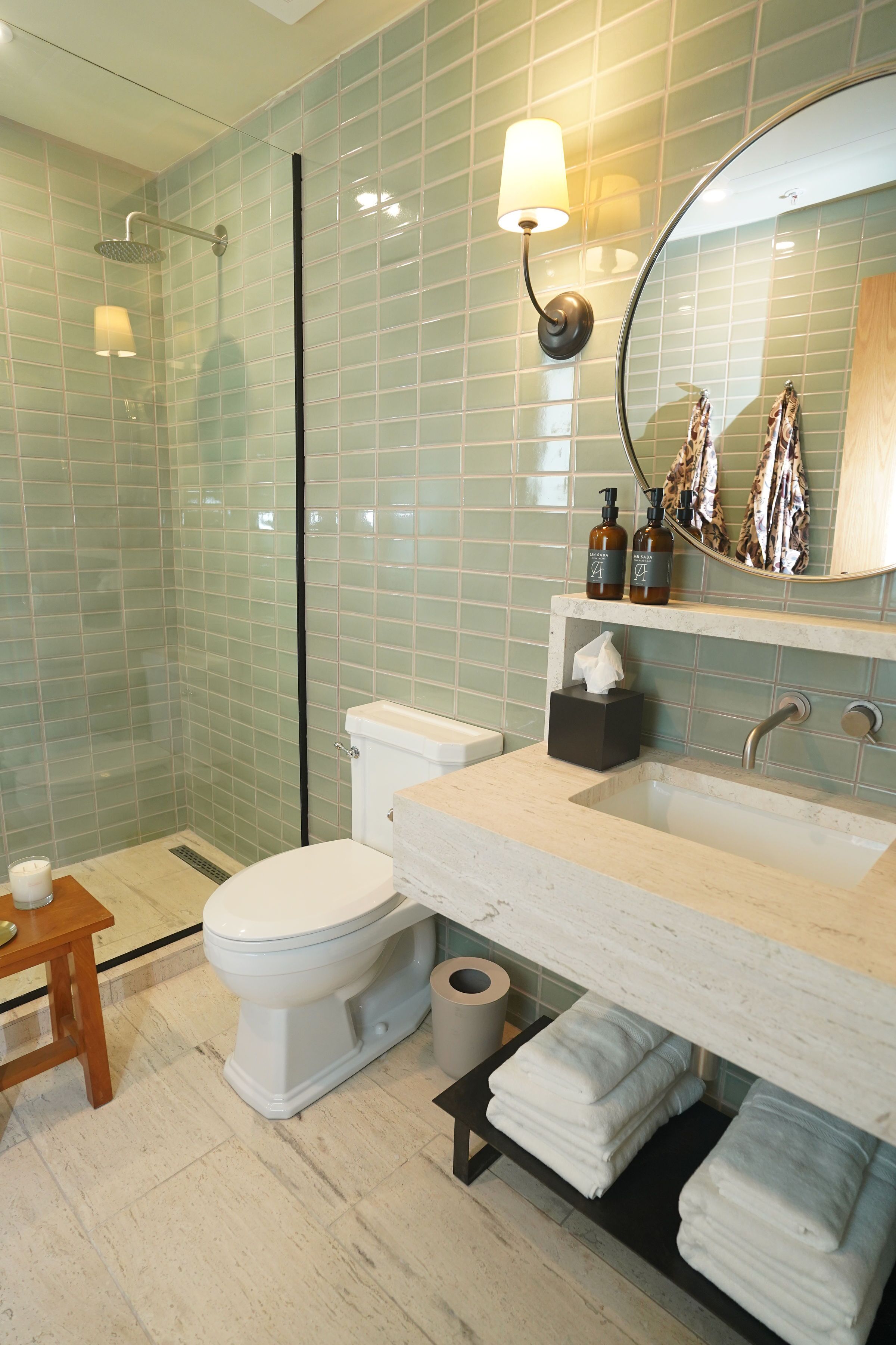 Un baño con cabina de ducha de vidrio, inodoro, lavabo con espejo y toallero con toallas.
