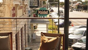 A balcony with a view of a street, a pharmacy sign, and parked cars. - Albert Hotel (Fredericksburg)