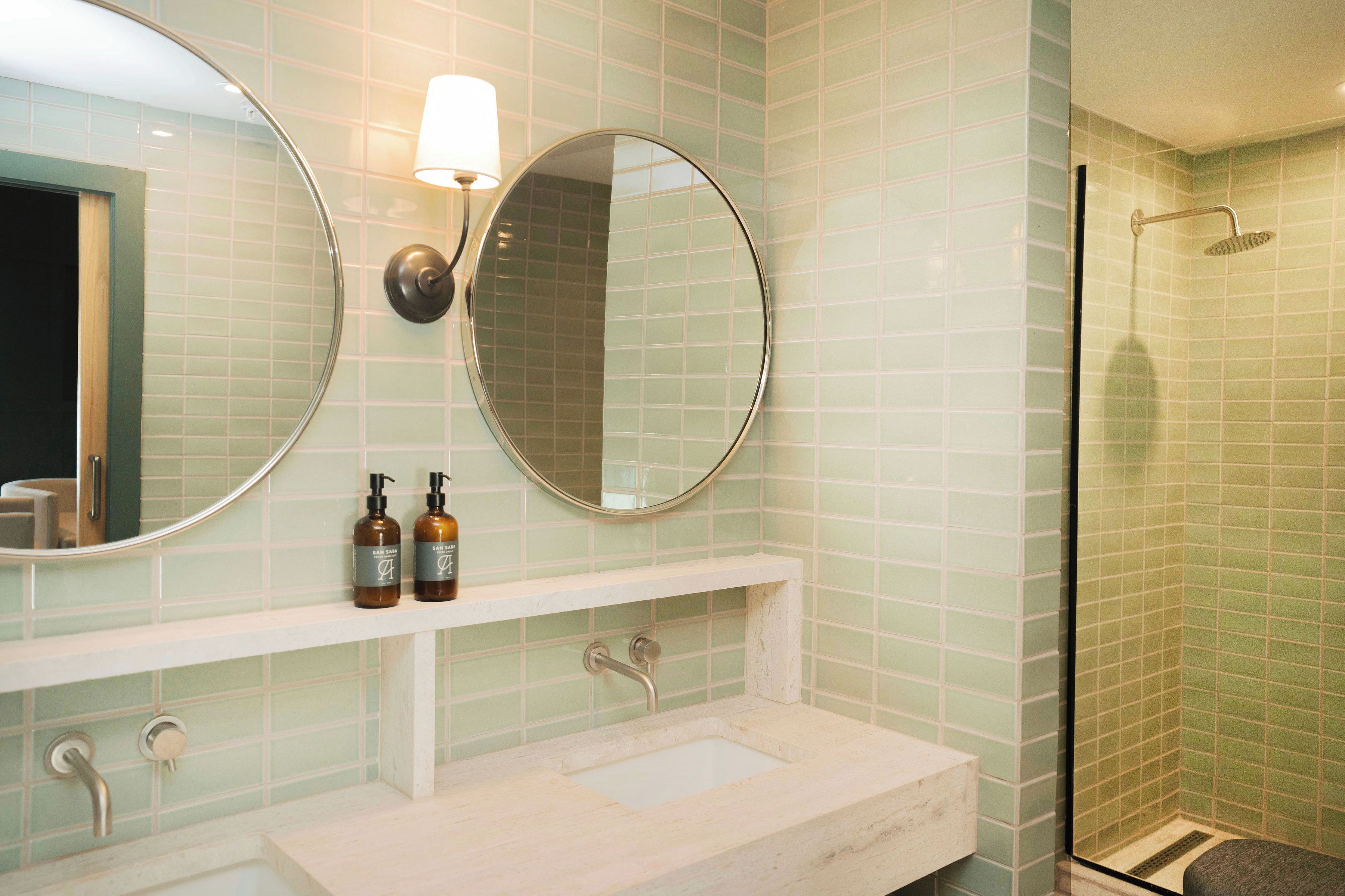 A bathroom with two round mirrors, a sink, and a shower.