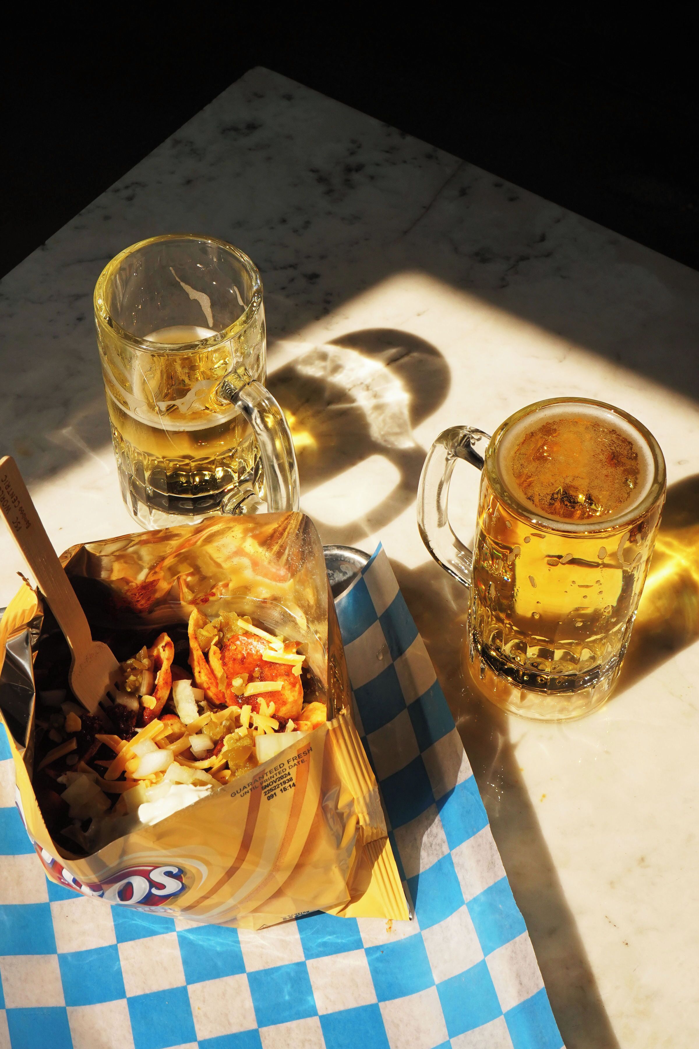 A table with a checkered paper, a beer mug, and a box of snacks.