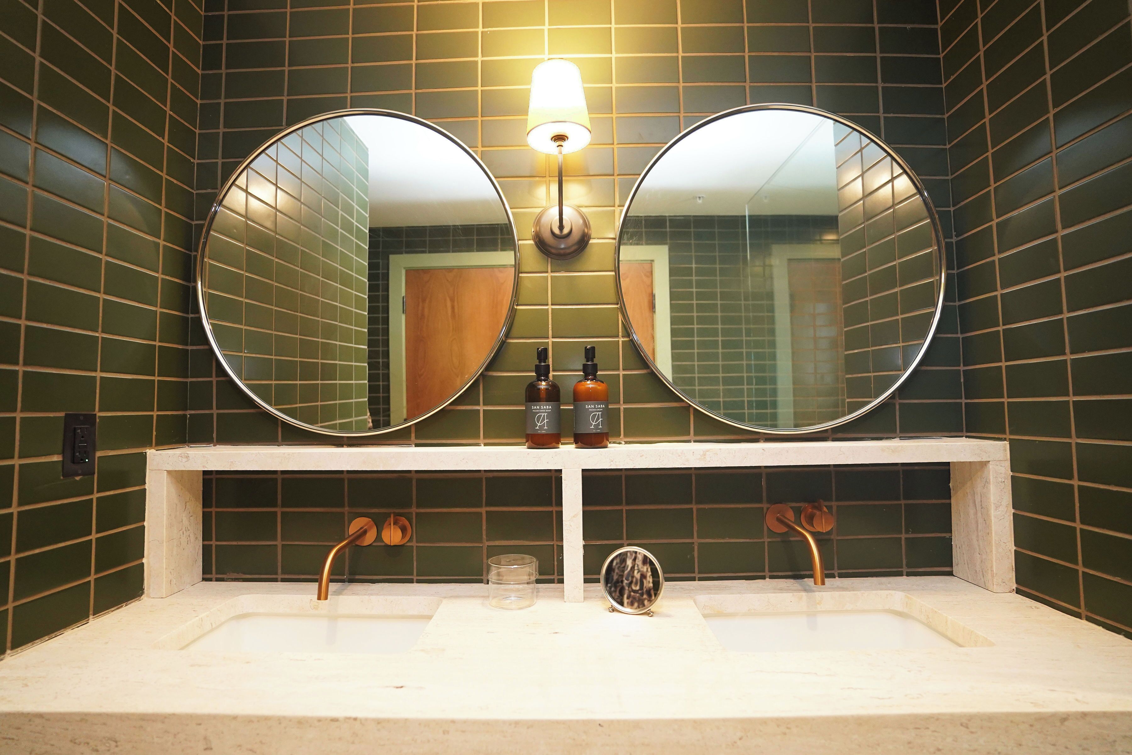 A bathroom with two round mirrors, a light fixture above, and a sink with two faucets.
