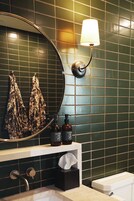 A bathroom with a round mirror, a wall-mounted lamp, a sink, and a towel rack with patterned towels.