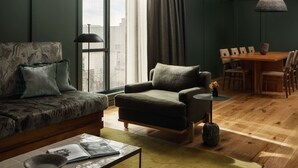 A modern living room with a sofa, armchair, dining table, and a large window. - Albert Hotel (Fredericksburg)