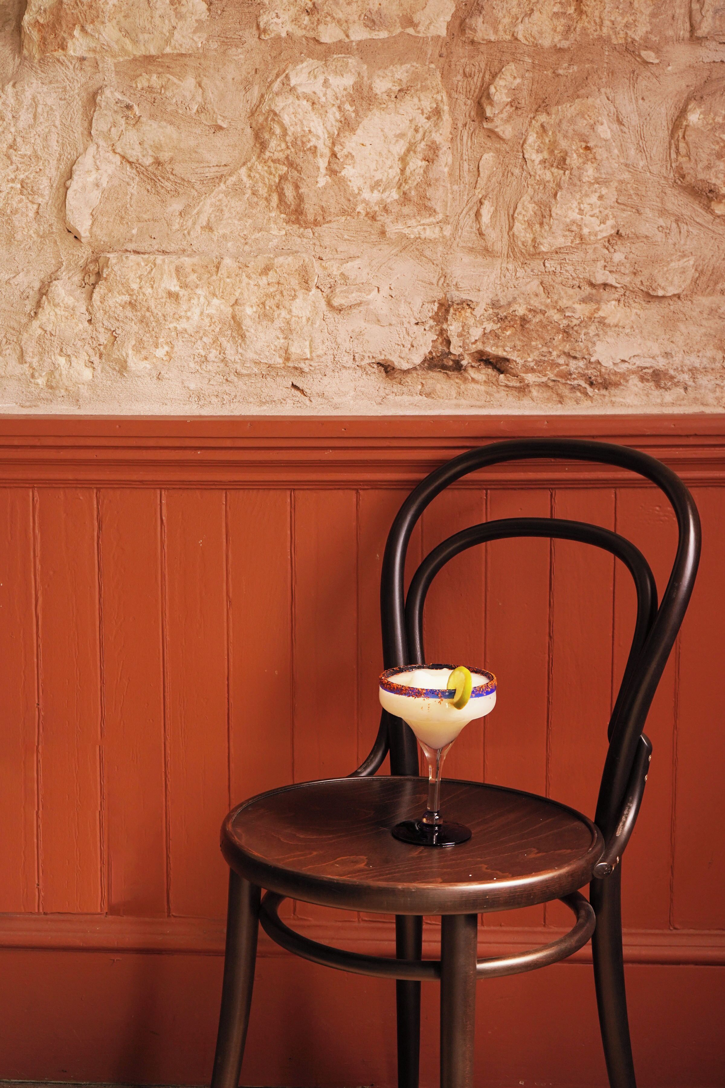 A chair with a drink in front of a textured wall.