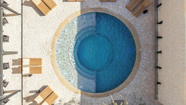 A circular pool with a stone border, surrounded by wooden lounge chairs and tables. - Albert Hotel (Fredericksburg)