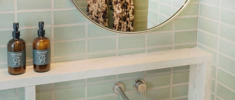 Un bagno con uno specchio rotondo, una lampada a parete e due flaconi sul ripiano.
